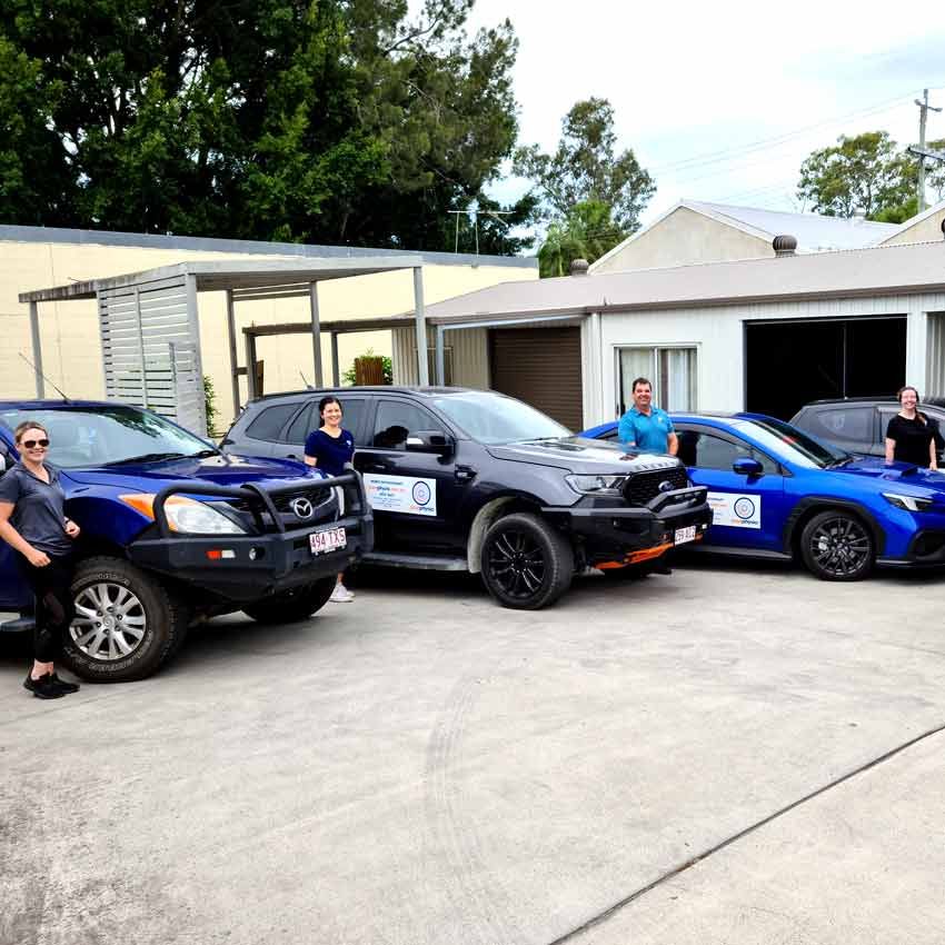 The Your Physio team standing with their branded mobile physiotherapy vehicles