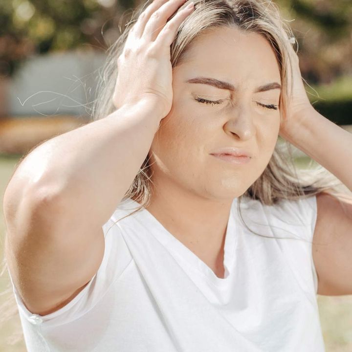 A woman outdoors holding her head with both hands
