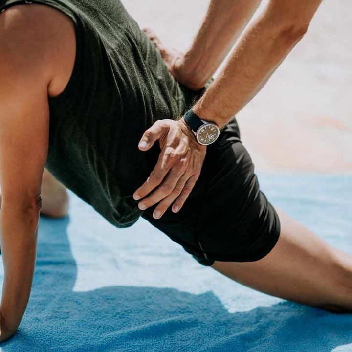 Physiotherapist guiding a patient through a hip mobility exercise on a mat